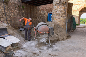 A man in an orange shirt is using a cement mixer