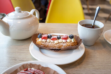 A pastry with strawberries and blueberries is on a plate next to a cup of tea