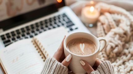 Woman holding latte cup working at laptop in cozy autumn or winter atmosphere with knitted plaid, candles and garland. Planning, distant work, freelance, education, online courses. Hygge. Faceless