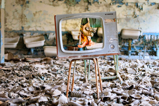 Ukraine, Pripyat, Chernobyl. Gas masks, many of them child-sized, litter the floor of an abandoned school. One has been placed over a doll's head. Seen through an empty television screen.