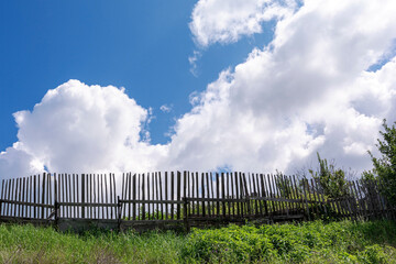 A rustic scene of an old wooden fence against a backdrop of a blue sky with fluffy clouds.