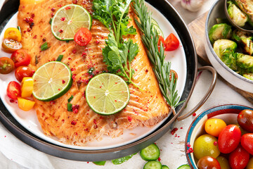 Grilled salmon and vegetables on wooden light background. Dinner table with cooked fish, tomatoes, asparagus