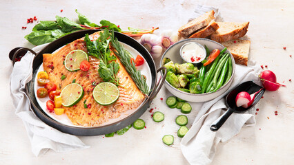 Grilled salmon and vegetables on wooden light background. Dinner table with cooked fish, tomatoes, asparagus