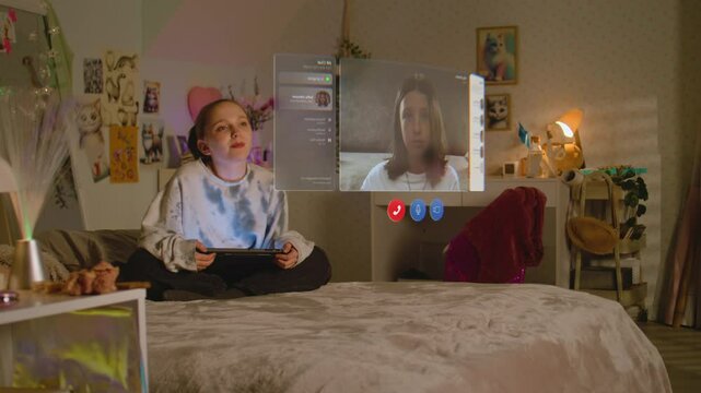 Teenager girl uses tablet computer, talks to friend in AR chat app using virtual reality, sits on bed at home. VFX graphics of holographic video call interface. Futuristic metaverse. Augmented reality