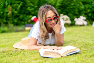 Woman Reading Book While Lying on  Grass in Sunny Backyard During Summer