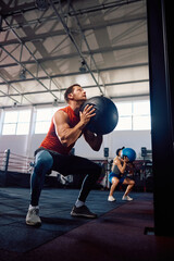 Athletic man using medicine ball for squat and throw exercise during cross training in a gym.