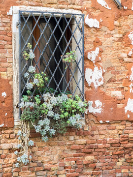 Italy, Venice. An old Venetian brick wall with flaking plaster along one of the canals inset with an equally old window.