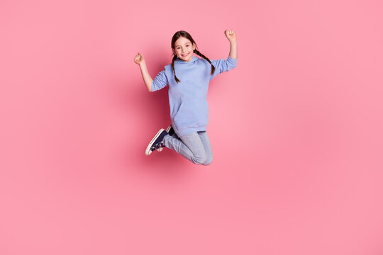 Full size photo of lovely small schoolkid jump raise fists wear hoodie isolated on pink color background