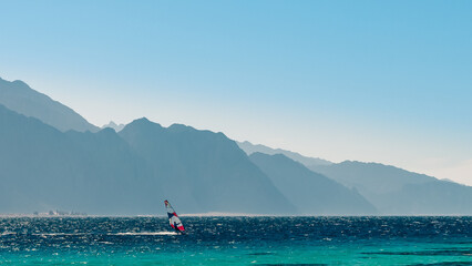 surfer rides in the Red Sea against the backdrop of high rocky mountains and a blue sky with clouds in Egypt Dahab