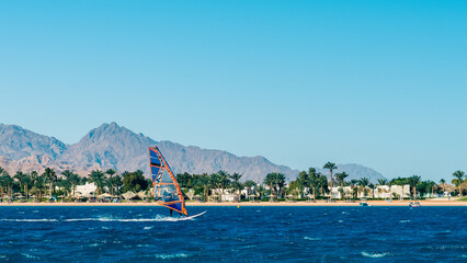 windsurfer rides in the sea on the background of the beach with palm trees and high rocky mountains...