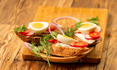 Sandwiches with tomatoes, onions and eggs lie on a wooden plate. Sandwiches on a wooden cutting board. Proper nutrition.