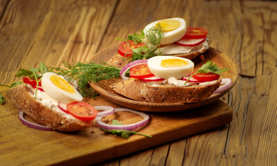Sandwiches with tomatoes, onions and eggs lie on a wooden plate. Sandwiches on a wooden cutting board. Proper nutrition.