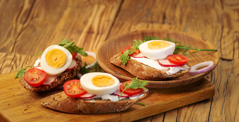 Sandwiches with tomatoes, onions and eggs lie on a wooden plate. Sandwiches on a wooden cutting board. Proper nutrition.