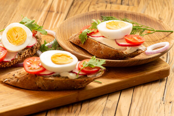 Sandwiches with tomatoes, onions and eggs lie on a wooden plate. Sandwiches on a wooden cutting board. Proper nutrition.