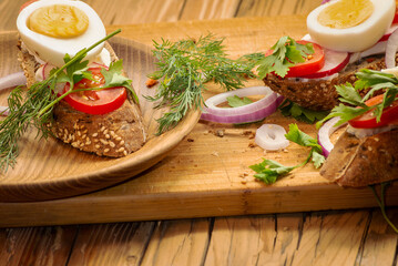 Sandwiches with tomatoes, onions and eggs lie on a wooden plate. Sandwiches on a wooden cutting board. Proper nutrition.