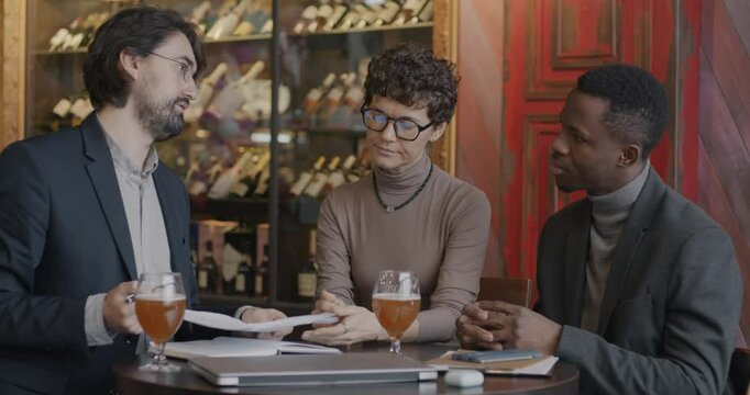 Two businessmen African American and Middle Eastern negotiating a deal then signing contract while female interpreter translating talks in cafe. Business and cooperation concept.