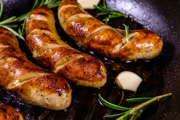 Roasted sausages with rosemary twigs and garlic in a cast iron grill pan