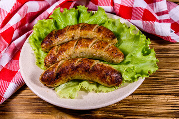 Plate with roasted sausages and lettuce leaves on a wooden table