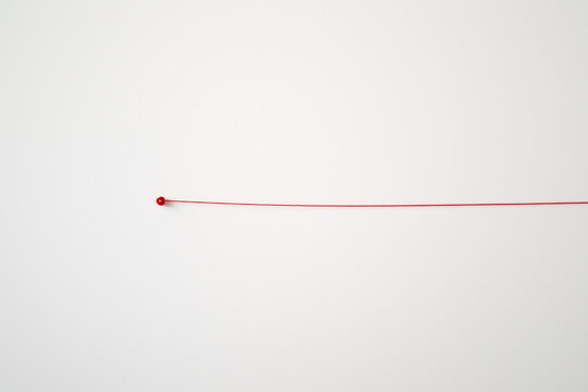 A red string is stretched out on a white wall
