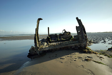 An abandoned half buried rusting and barnacle encrusted 4x4 left to fall apart on a wet sandy beach.