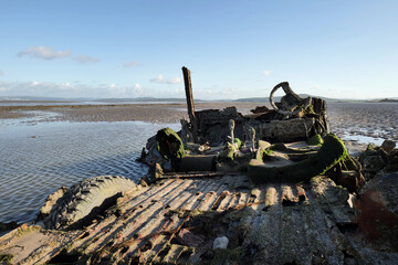 An abandoned half buried rusting and barnacle encrusted 4x4 left to fall apart on a wet sandy beach.