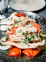 Plate of fresh salad featuring shredded tuna, sliced tomatoes, onions, and parsley, served on a dark plate
