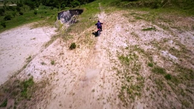 Aerial view from FPV drone. Next shot of a professional motocross rider riding his FMX motorcycle on extreme off-road terrain