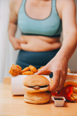 To eat or not. Cheerless plump woman looking at the burger while thinking to eat it or not