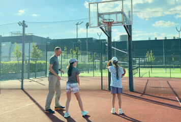 summer holidays, sport and people concept - happy family with ball playing on basketball playground