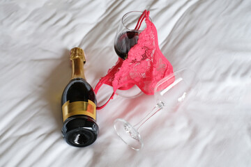 Romantic sex date, red lace panties and wine glasses on the bed. Concept of night of passion, female lingerie. Woman accessories.