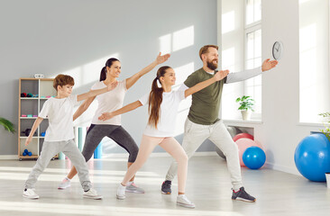 Parenthood and sport lifestyle. Happy active husband, wife and their two children doing family yoga session together. Family in comfortable clothes performs standing in same pose in bright home gym.