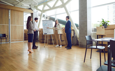 Business team has discussion near white board flip chart during brainstorming session in meeting room. Male and female colleagues discuss ideas for new development strategy. Concept of teamwork.