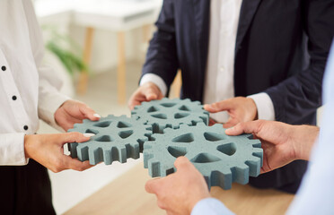 Business people standing connecting cogs wheel, hands close-up. Concept of partnerships in...