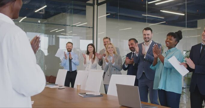 Employees of marketing agency or big financial company celebrate success and applaud during a work meeting. Woman speaker receives a standing ovation after her presentation at a corporate team meeting