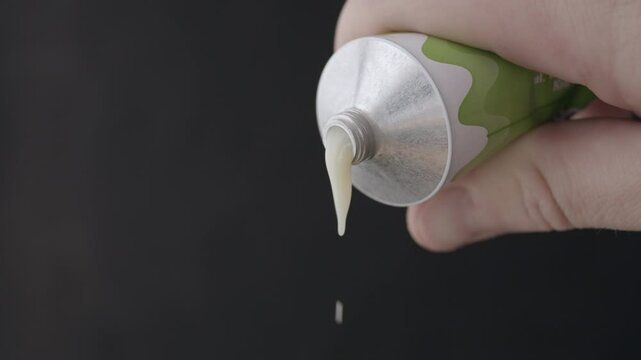 Condensed milk pours from a tube. Hand holds and squeezes a tube full of condensed milk. Close up.