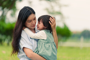Fototapeta premium mother holding and comforting her crying toddler baby girl on grass field in park
