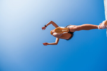 Young female athlete leaps over a hurdle in a parkour workout under a clear blue sky
