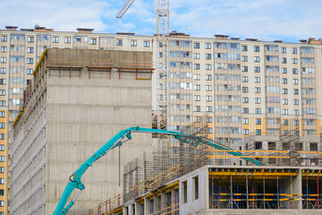 Pouring cement on the floors of residential multistory building under construction using a concrete pump truck with high boom to supply the mixture to the upper floors