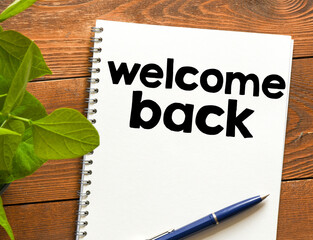 WELCOME BACK words written in a notebook on a wooden table. View from above.