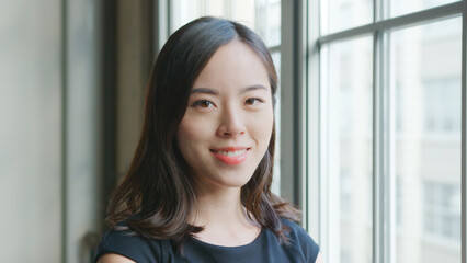 Head And Shoulders Portrait Of Smiling Young Businesswoman Standing By Window In Office