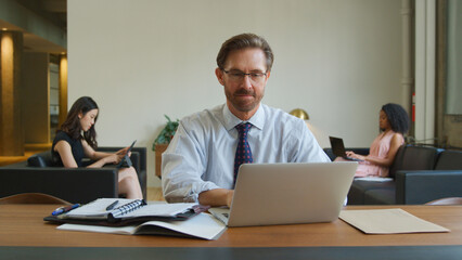 Mature Businessman In Informal Seating Area Of Modern Office Working On Laptop 