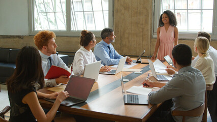 Young Businesswoman Giving Presentation To Multi-Cultural Team Sitting Around Table In Modern Office