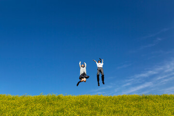 菜の花の咲く土手でジャンプをする男女の高校生。春、入学、お祝い,卒業,合格イメージ