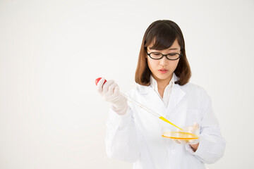 シャーレにピペットで試薬を注ぐ白衣を着た若い女性