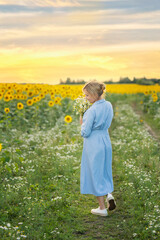 Fototapeta premium happy woman with a bouquet of daisies walking along a dirt road in a field of sunflowers
