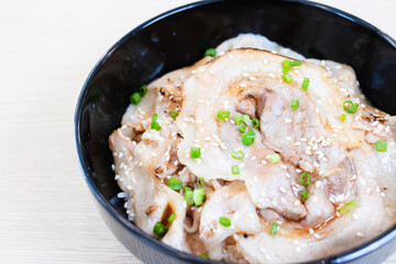 Donburi rice topped with chashu pork slices  in a black bowl.