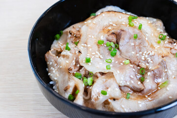 Donburi rice topped with chashu pork slices  in a black bowl.