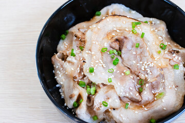 Donburi rice topped with chashu pork slices  in a black bowl.