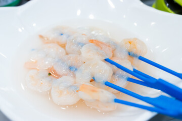 Fresh white shrimp with tails left on, skewered on blue sticks and placed on a white plate.
