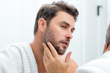 Obraz premium Millennial hispanic man looking in mirror, facial skin and stubble. Male beauty care product. Skincare, home spa. Beauty portrait of a beautiful man. Spa model, moisturizing nourishing creme.